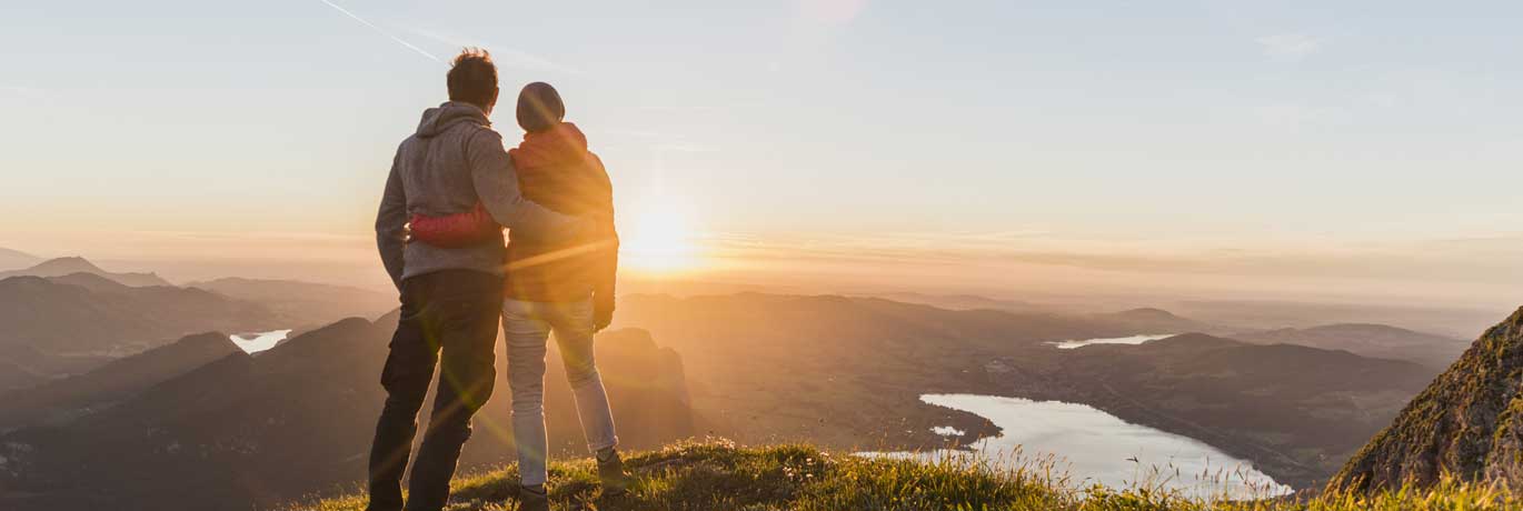 A man and woman standing on a mountain watching the sunset